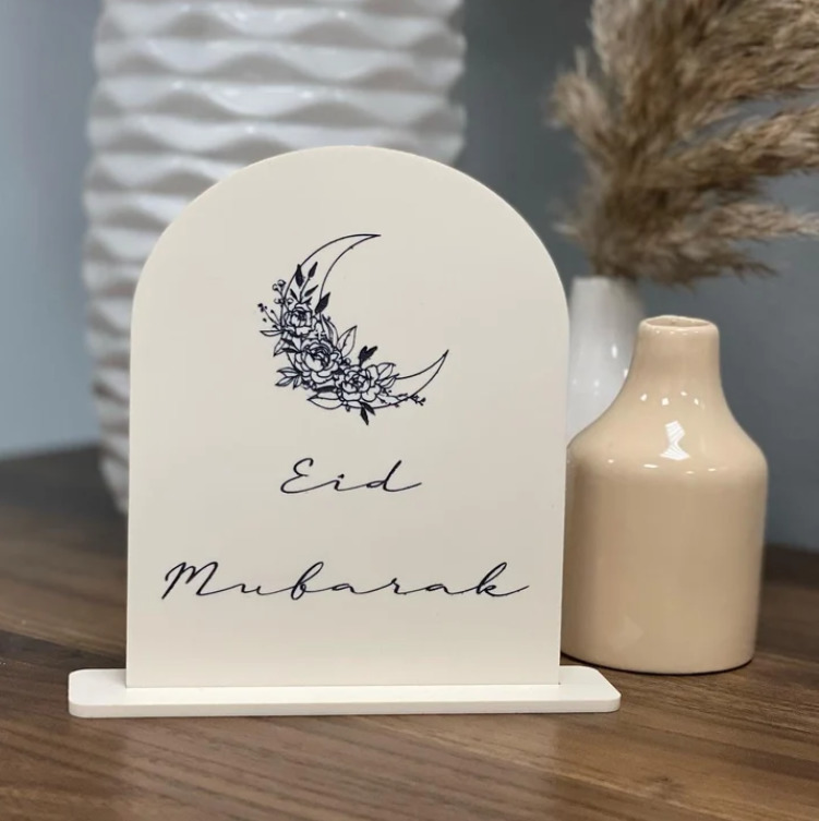 Acrylic tabletop sign that reads Eid Mubarak with additional vases on table