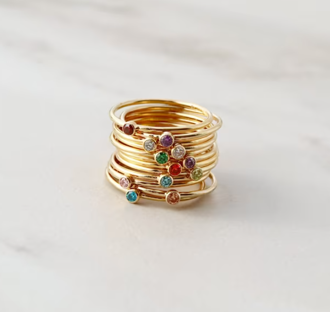 Gold rings with birthstone gems stacked in one pile for Mother's Day gifts